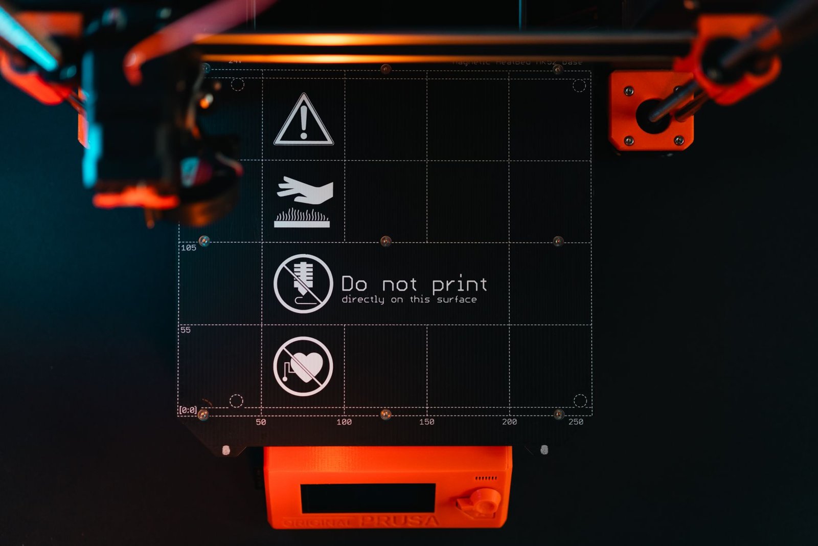 3D printer build plate with warning symbols, showcasing high-tech equipment in a workspace.