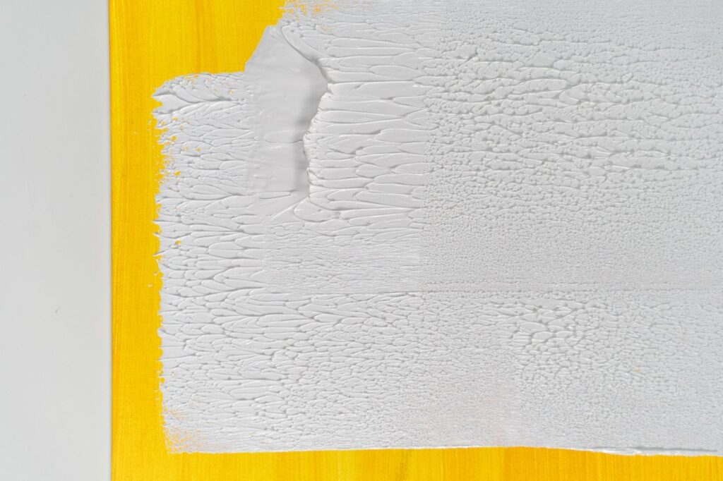 Close-up of a textured acrylic abstract painting featuring white and yellow colors.