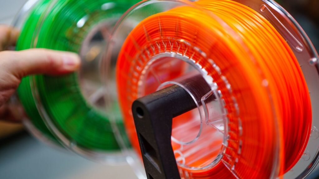 Vibrant orange and green 3D printer filament spools for innovative manufacturing uses.
