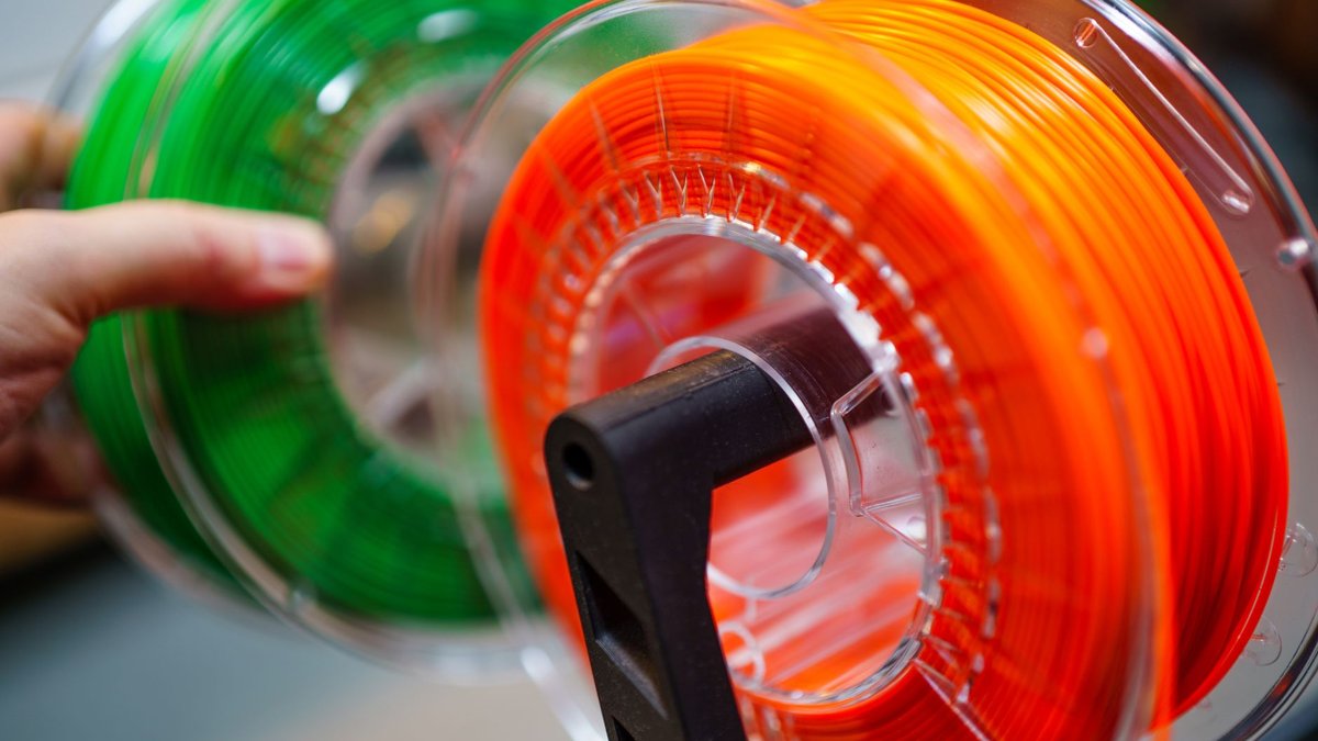 Vibrant orange and green 3D printer filament spools for innovative manufacturing uses.