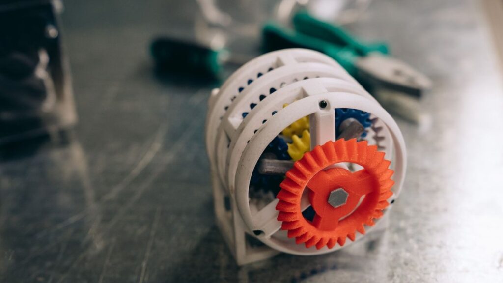 A close-up photo of a 3D printed gear mechanism on a metallic workbench, highlighting innovation and technology.