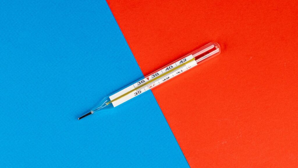 Glass thermometer on a vibrant red and blue background, symbolizing health and temperature measurement.