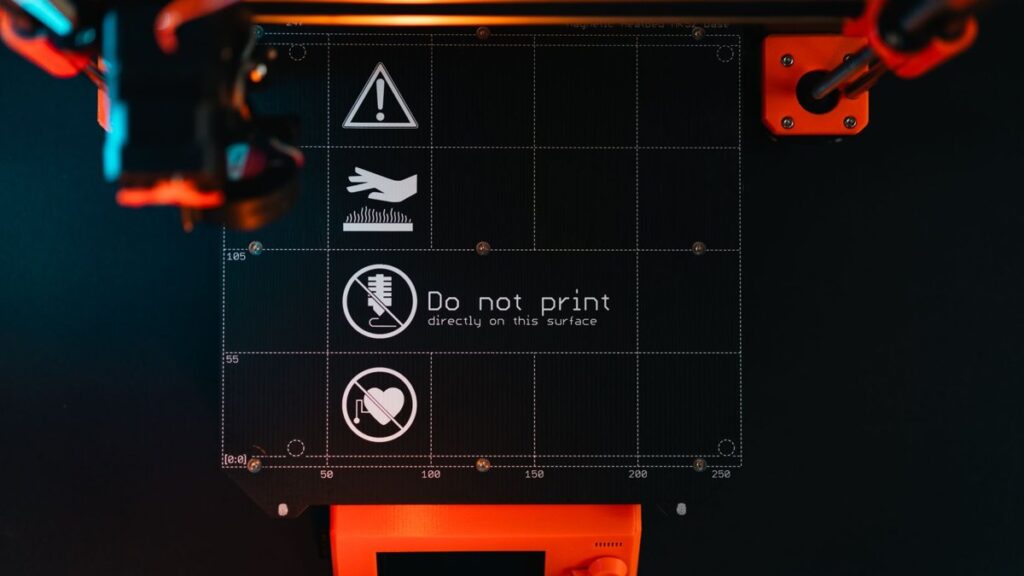 3D printer build plate with warning symbols, showcasing high-tech equipment in a workspace.