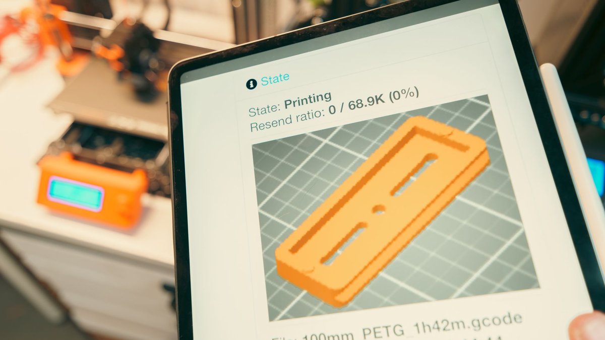 Close-up of a digital tablet displaying a 3D printing process in a workshop setting.
