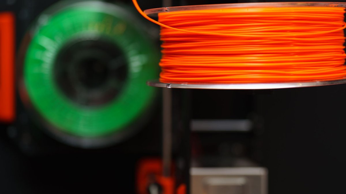 Detailed view of orange and green 3D printer filament spools, perfect for creative and industrial projects.