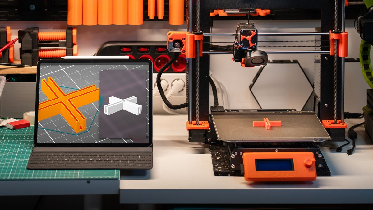 Workspace featuring a 3D printer and computer showcasing 3D models, illustrating modern technology in action.